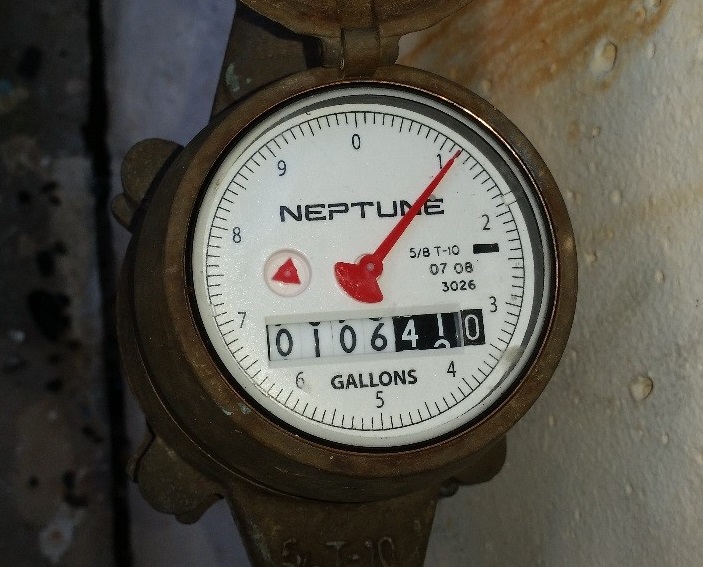 A water meter typical of one found in Belleair with a white face and a red needle.