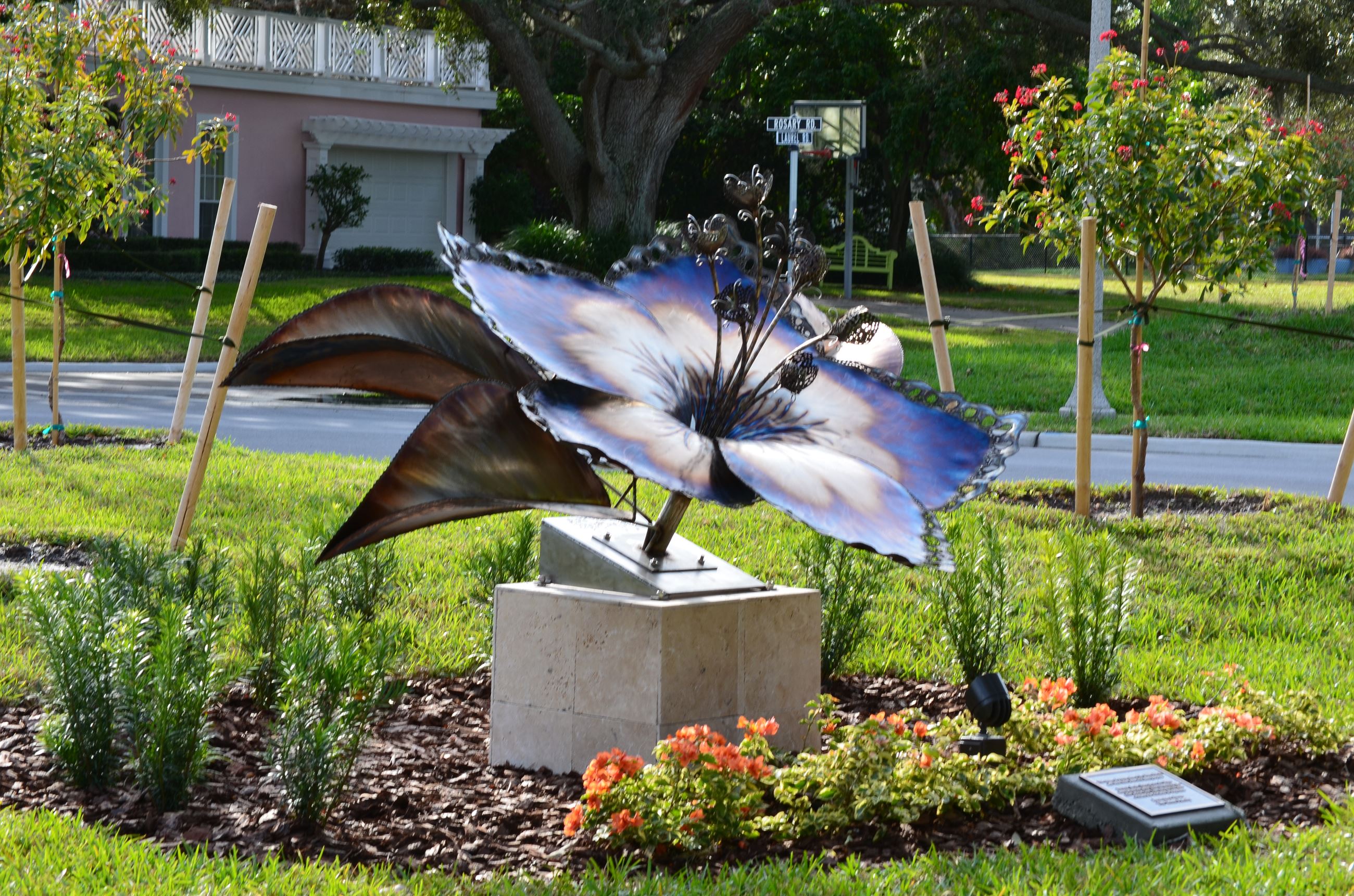 A large metal iridescent sculpture of an azalea flower that is in Pat Wall Park