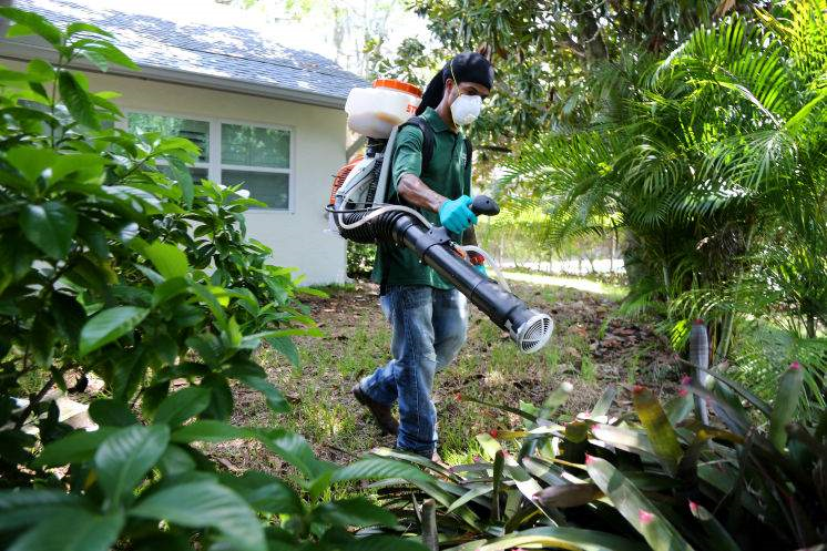 Pinellas County Mosquito Control employee wearing a mask and using a machine to spray for mosquitos