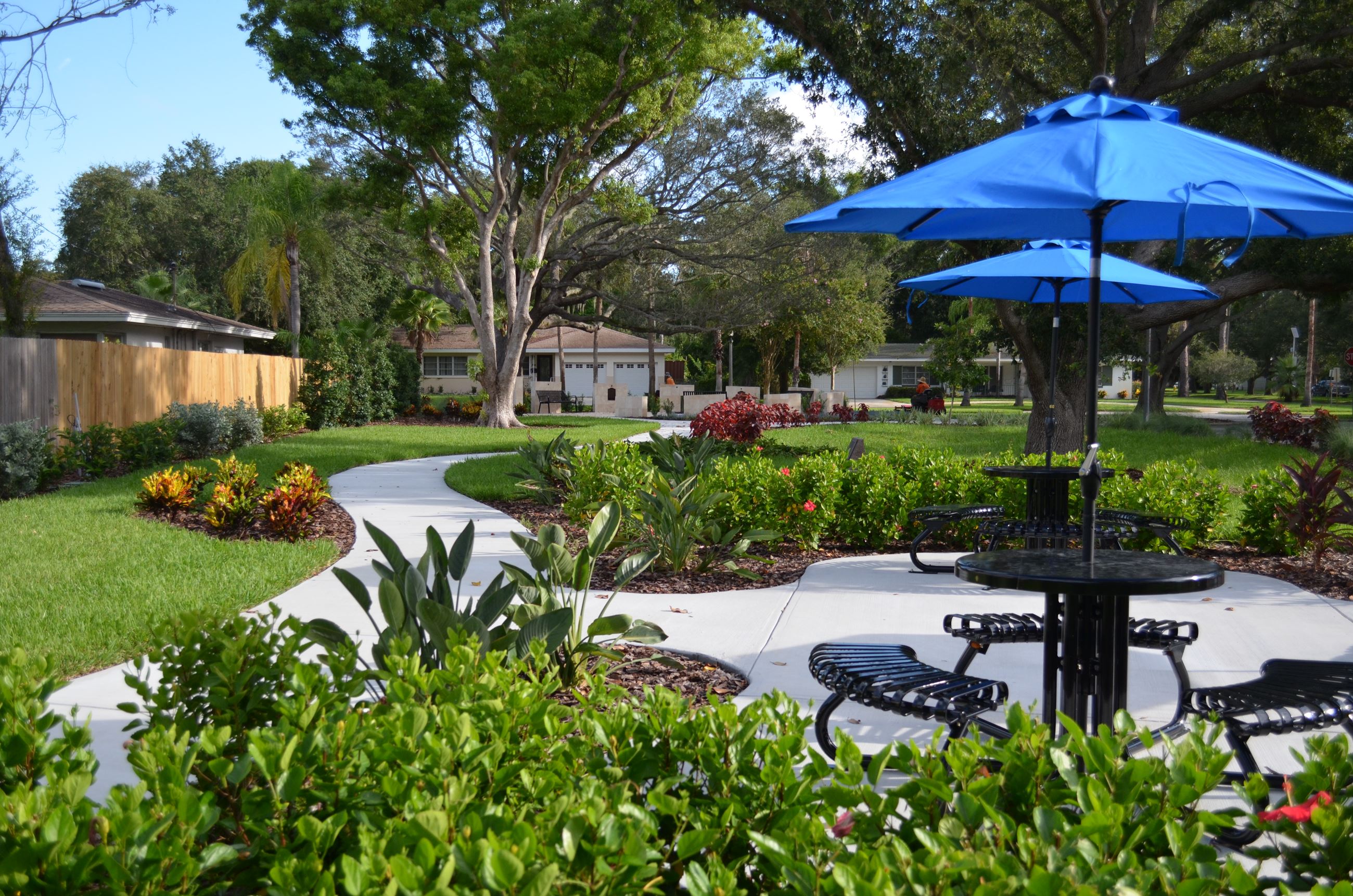 A view of Jeffery W. Tackett Park with blue umbrellas over black picnic tables and landscaping in th