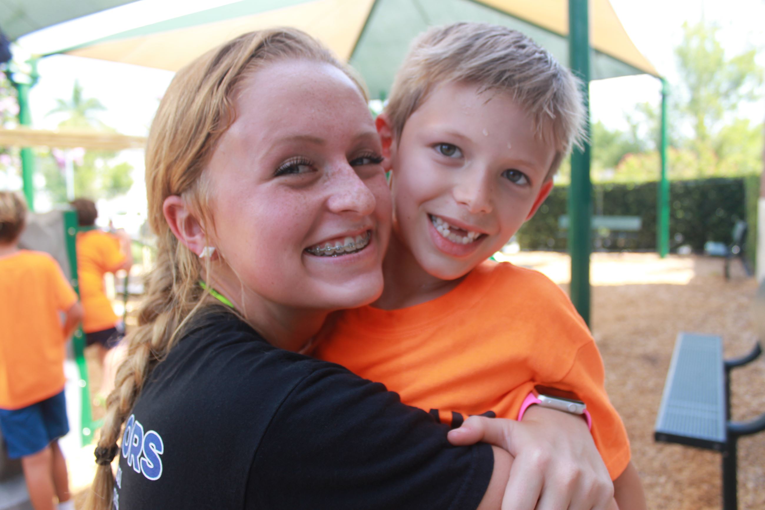 A boy and girl hugging, both smiling at the camera. 