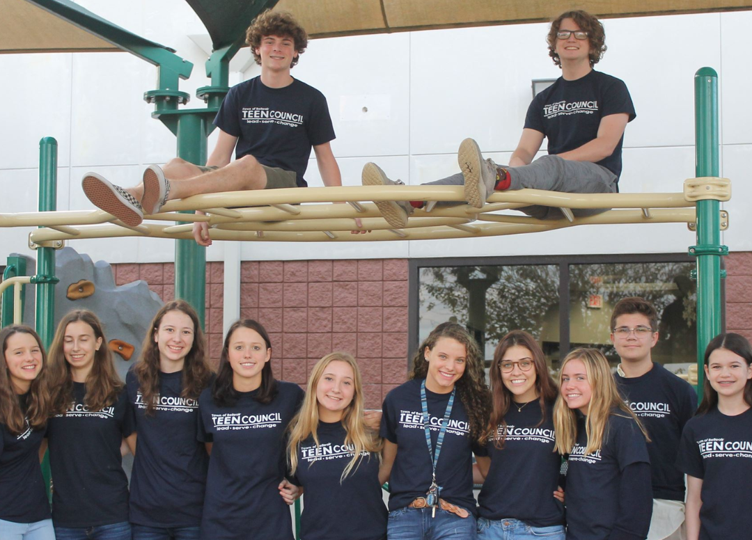 A group of teens smile proudly as they pose for a photo in their blue youth council t shirts.