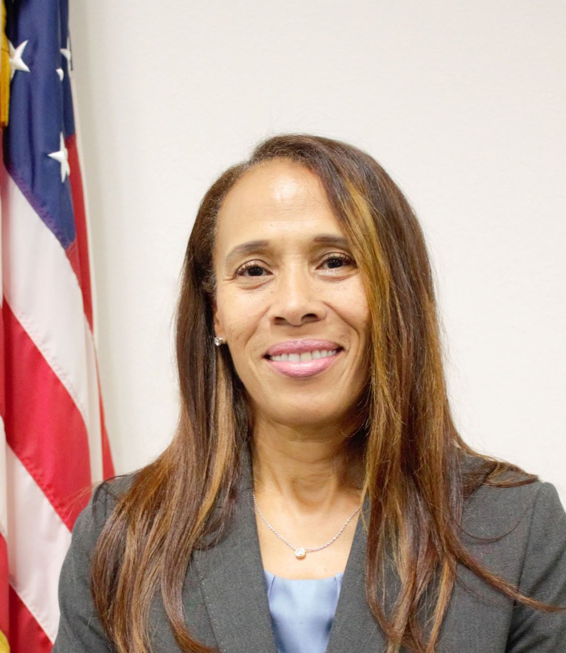 Commissioner Barris smiles with the American flag behind her. 