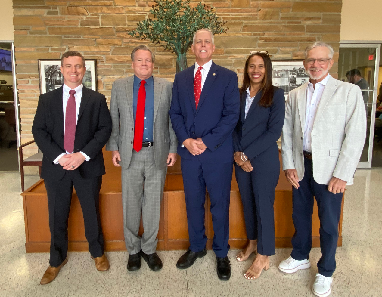The Town of Belleair Commission (mayor and four commissioners) are smiling in the Town Hall lobby.